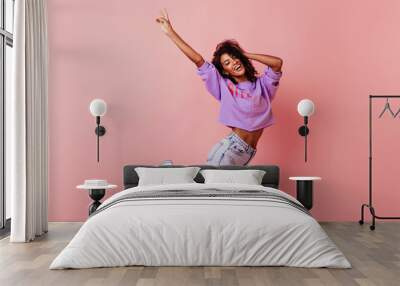 Shapely jocund girl dancing on rosy background. Good-humoured african lady jumping with smile. Wall mural