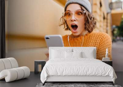 shocked girl with brown eyes looking at phone screen with mouth open. outdoor portrait of surprised  Wall mural