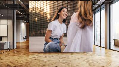 Smiling young caucasian woman in good mood spend their leisure time sitting near university. Brunette laughs, wears t-shirt and jeans. Summer lifestyle concept Wall mural