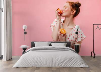 Snapshot of charming girl dressed in dress with cherry print. Woman with yellow eyeshadows holds oranges and looks into camera Wall mural