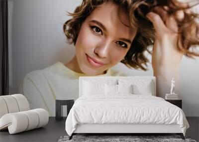 Studio shot of charming caucasian girl isolated on white background. Indoor portrait of pretty lady playing with short dark hair with gently smile. Wall mural