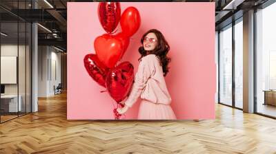 Studio shot of sensual ginger girl with red heart shaped balloons. Indoor photo of beautiful woman isolated on pink. Wall mural