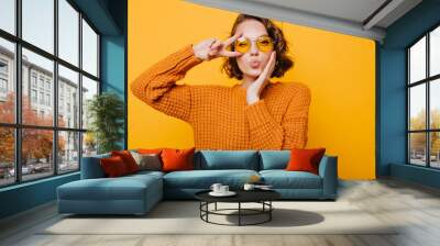 Stunning short-haired female model posing with kiss face expression on yellow background. Close-up portrait of stylish european girl standing with peace sign in front of wall. Wall mural