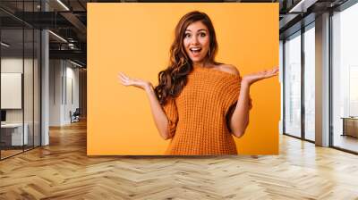 Surprised beautiful woman posing on bright yellow background. Lovely brunette girl standing in studio with amazed face expression. Wall mural