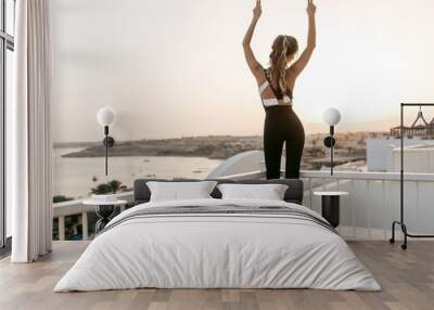 View from back joyful amazing woman in sportswear stretching to sunrise on seafront.  Sunny morning, tropical country, true emotions, relaxation on sea, healthy lifestyle. Place for text Wall mural