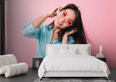 Wonderful asian girl with happy face expression waving hair while listening music. Cute hispanic female model chilling on pink background with favorite song. Wall mural