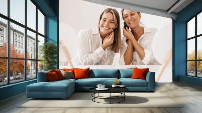 Young caucasian women doing facial massage with scraper in front of mirror on white background. Blondes wear shirts using gouache jade stone at home. Cosmetic products, concept Wall mural