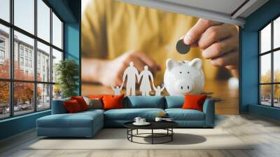 businessman putting coin on the piggybank and paper family on table, donation, saving, charity, fami Wall mural