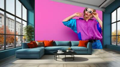 Cool teenager. Fashionable DJ girl in colorful trendy jacket and vintage retro sunglasses enjoys style of 80s � 90s vibes. Teenager Girl at disco party. Young fashion model on pink color background. Wall mural