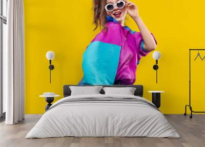 Cool teenager. Fashionable DJ girl in colorful trendy jacket and vintage retro sunglasses enjoys style of 80s � 90s vibes. Teenager Girl at disco party. Young fashion model on yellow color background. Wall mural