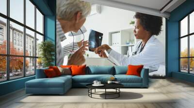 A female black ethnicity doctor sits at her office and examining elderly female patient Wall mural