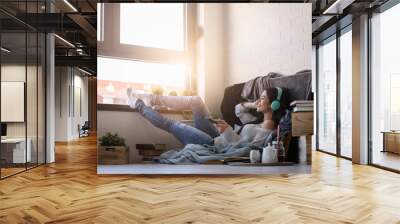 Beautiful young woman at home enjoys listening music through headphones Wall mural