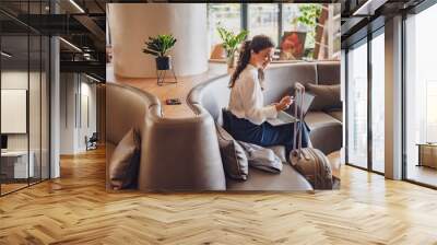 Businesswoman sitting in a hotel lobby, using laptop. Woman working on a business trip using online connections. Business lady went to business trip and stayed at the hotel. Wall mural