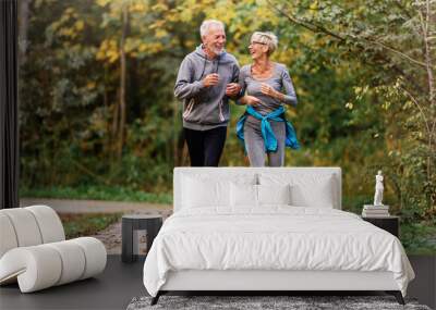 Cheerful active senior couple jogging in the park. Exercise together to stop aging. Wall mural