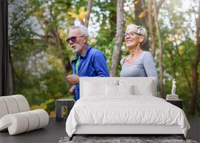 Cheerful active senior couple jogging in the park. Exercise together to stop aging. Wall mural