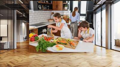 Children helping mother in the kitchen preparing tasty salad. Healthy fresh homemade food. Chores for children. Wall mural