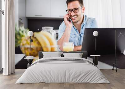 Handsome man using laptop computer at home, drinking juice and coffee in the morning. Working From Home. Wall mural