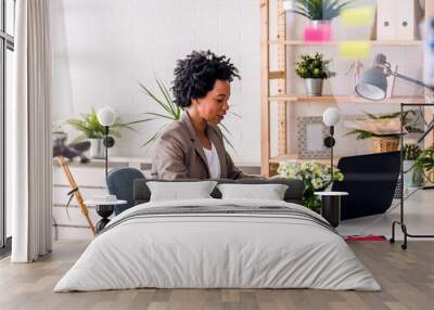 Happy smiling african-american business woman working on laptop at office. Businesswoman sitting at her working place Wall mural