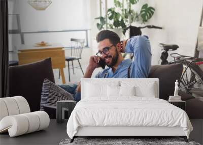 Happy smiling man using smartphone working on laptop computer while sitting on sofa at home Wall mural