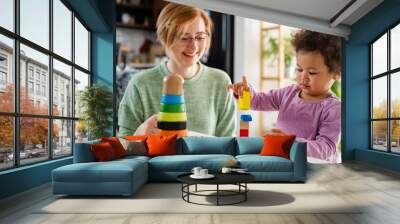 Mother looking at a child playing with an educational didactic toy. Young woman and child playing with didactic toys Wall mural