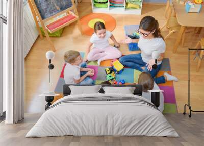 Preschool teacher talking to group of children sitting on a floor at kindergarten Wall mural