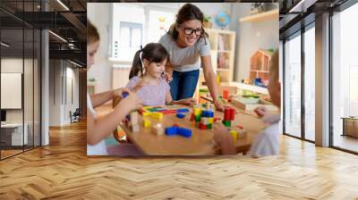 Preschool teacher with children playing with colorful wooden didactic toys at kindergarten Wall mural