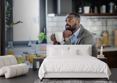 Thoughtful African-American man in business attire enjoying a cup of coffee in a modern kitchen, taking a quiet moment before work. He appears reflective and calm. Wall mural