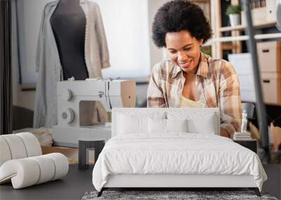 Young African-American entrepreneur woman working in her small workshop using smartphone. Online banking apps for entrepreneurs Wall mural