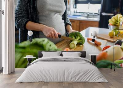 Young pregnant woman preparing healthy food with lots of vegetables at home kitchen Wall mural