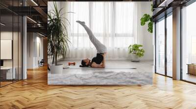 Young woman practicing yoga exercise at home. Daily sports routines for a healthy lifestyle and stress relief. Wall mural