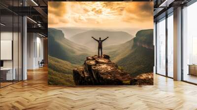 Man with raised hands standing on the edge of cliff and looking into the distance at sunset Wall mural