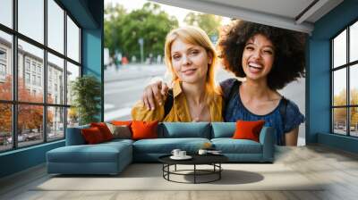 Couple of young women hugging each other at sunset on a summer day in the city - Millennials have fun together laughing and joking Wall mural