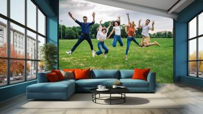 Group of five friends jump into the air with their hands up - Millennials have fun together at the park in the summer Wall mural