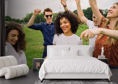 Group of friends at the park dancing under a rain of confetti - Millennials have fun in a public garden in summer at sunset Wall mural