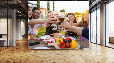 Group of friends celebrating in the garden in front of the house toasting a table set with glasses of red wine - Young people having fun together laughing and joking on a summer evening - Copy space Wall mural