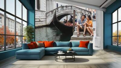 Loving couple on vacation in Venice, Italy - Millennials sitting on a canal with gondolas Wall mural