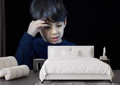 closeup portrait of latin boy looking down pensive and worry with one hand on his head. black background and copy space Wall mural