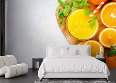 One glass of freshly pressed orange juice with a straw and mint leaves on a wooden board and light stone background. Top view, horizontal image, copy space Wall mural