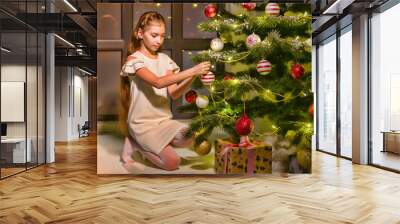 Little girl decorates a Christmas tree. New Year concept, family holidays. Wall mural