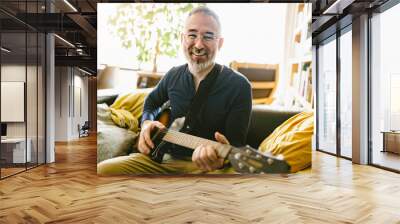 A attractive and relaxed looking man playing the guitar Wall mural