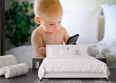 A portrait of a cute baby checking smartphone lying in a bed Wall mural