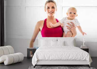 A Portrait of beautiful young mother in sports wear with her charming little baby in training session Wall mural