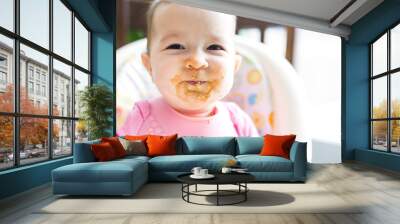 Adorable baby girl making a mess while feeding herself Wall mural