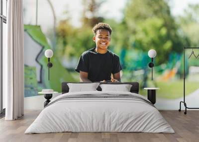 Afro-American boy with black t-shirt posing with his skateboard with the sky in the background Wall mural