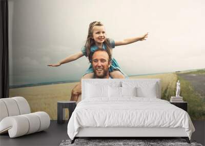 happy child girl and father are playing in wheat field. Wall mural