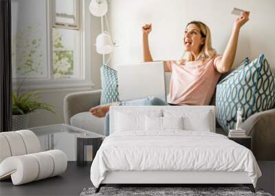 happy woman with a credit card and a laptop on sofa at home Wall mural