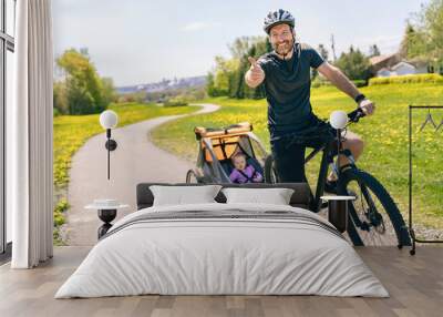 man riding a bicycle with a baby stroller attached to the bicycle. Wall mural