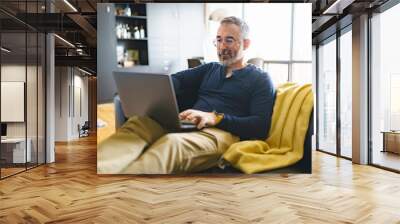 Portrait of handsome man with laptop on sofa Wall mural