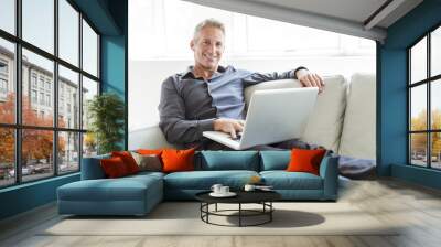 Portrait of happy mature man using laptop lying on sofa in house Wall mural