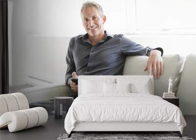 Portrait of mature man relaxing at home in sofa and cellphone Wall mural